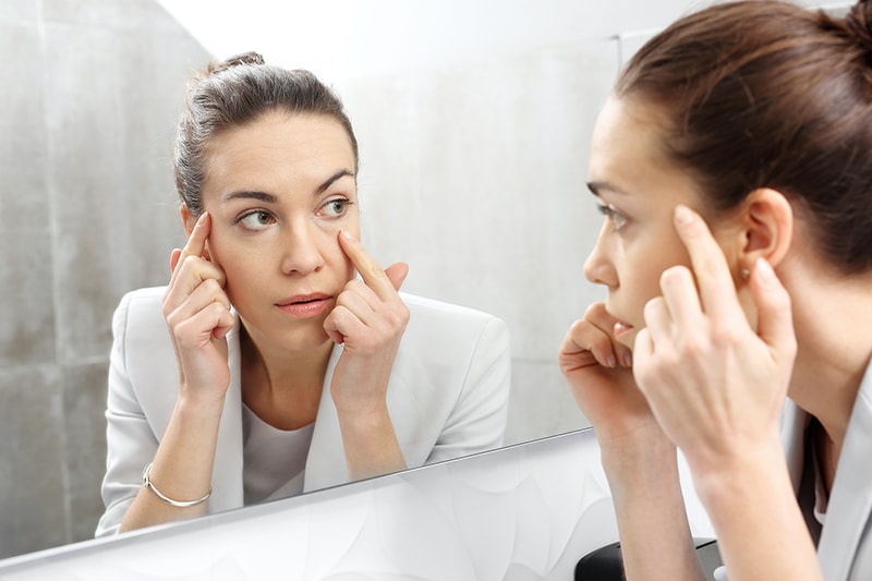 Woman looking at under-eye bags in mirror